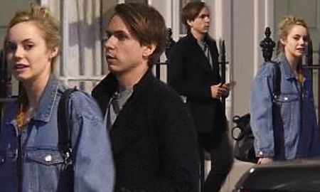 joe in a black coat, hannah with a tied up hair and jean jacket walking on the streets 